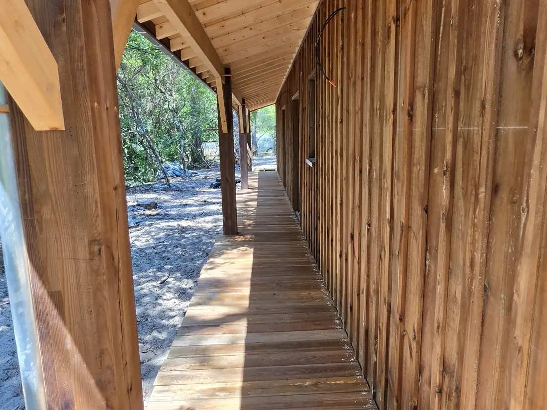Terrasse couverte longeant un bardage bois vertical, sous les pins — vue 2